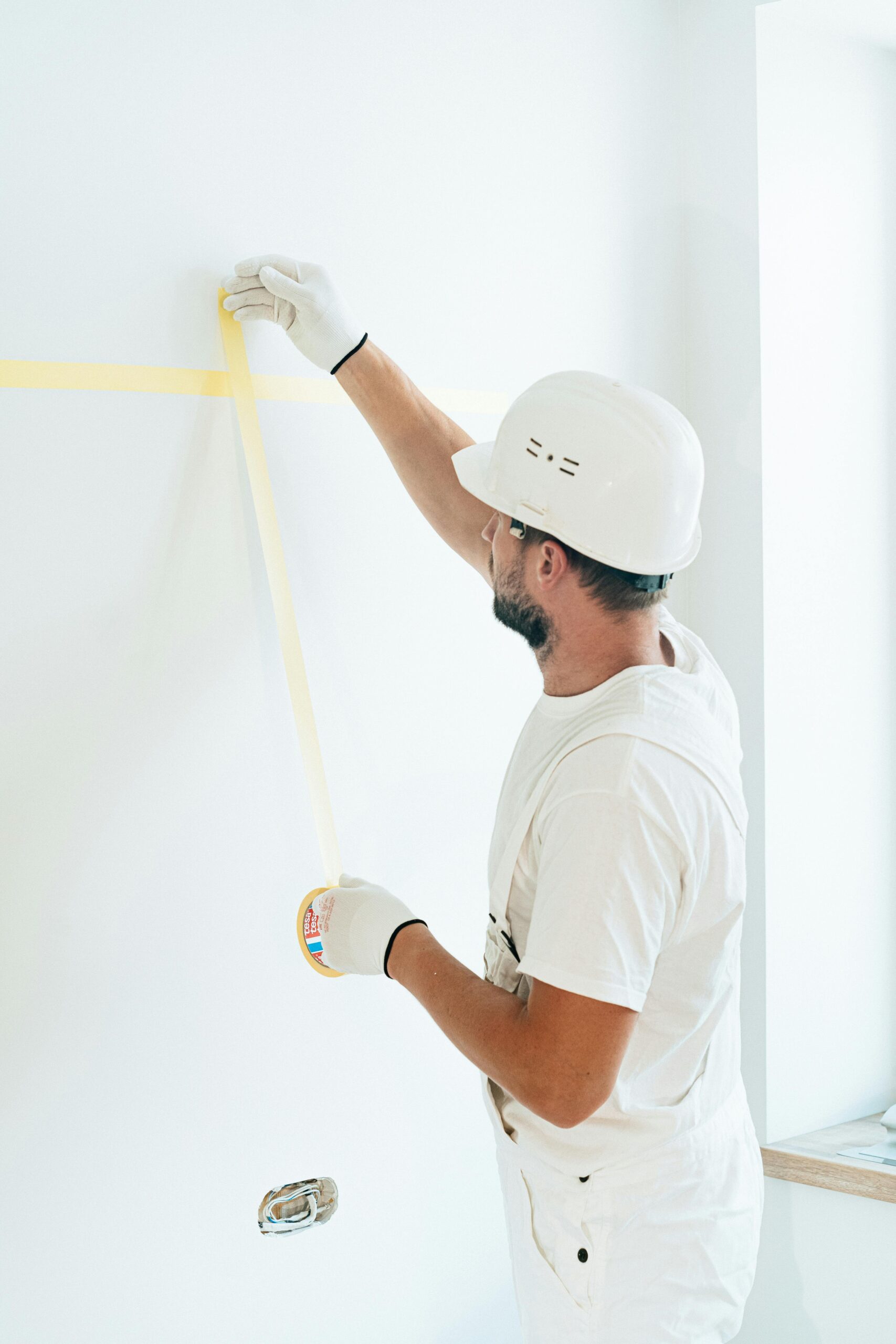 about-us Construction worker using tape to prepare wall surface, wearing safety helmet and gloves.